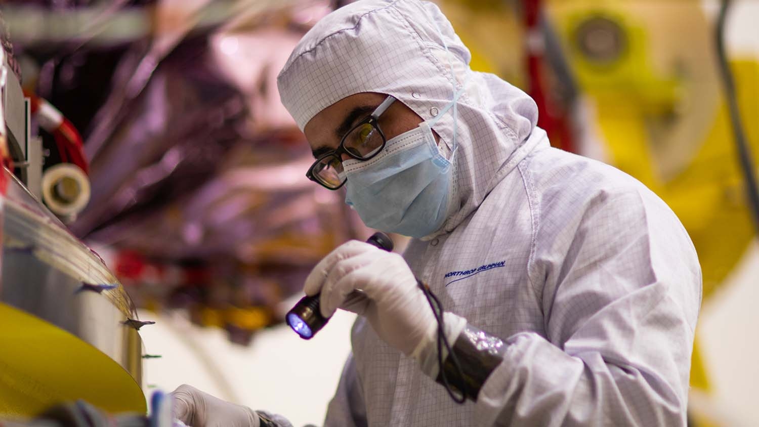 A man shines a flashlight over the James Webb Space Telescope